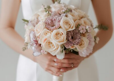 Braut hält einen eleganten Blumenstrauß mit Rosen und anderen Blumen in sanften Farben.