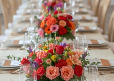 Bunte Hochzeits-Tischdekoration mit Blumenarrangements in verschiedenen Farben und Gläsern auf einem gedeckten Tisch.