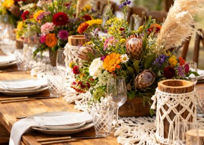 Tischdekoration mit bunten Blumenarrangements und Gläsern auf einem rustikalen Holztisch.