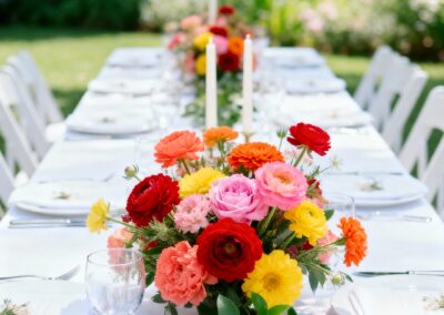 Tischdekoration mit bunten Blumenarrangements und Kerzen auf einem gedeckten Tisch im Freien.
